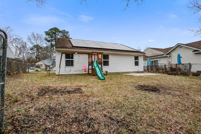 rear view of property featuring a patio, a playground, solar panels, fence, and a lawn