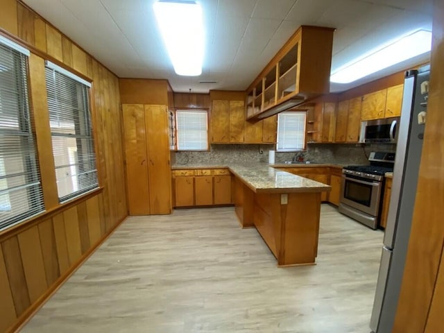 kitchen featuring appliances with stainless steel finishes, wooden walls, light wood-type flooring, and decorative backsplash