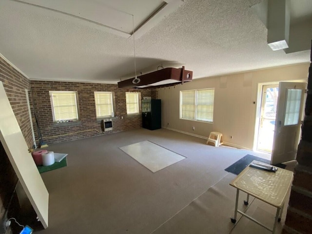 unfurnished living room featuring heating unit, brick wall, carpet flooring, and a textured ceiling