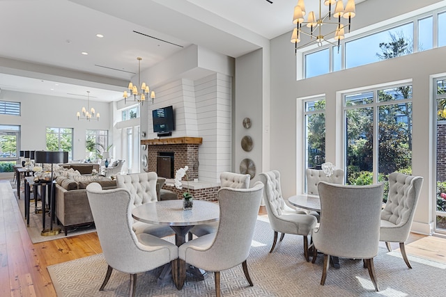 dining room with an inviting chandelier, a wealth of natural light, a fireplace, and light hardwood / wood-style floors