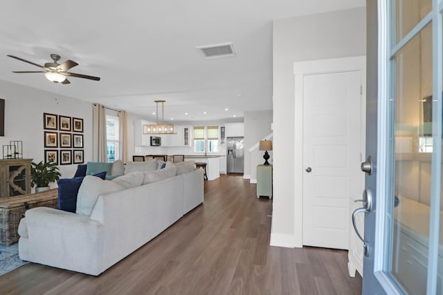 living room featuring recessed lighting, ceiling fan with notable chandelier, visible vents, and dark wood-style flooring