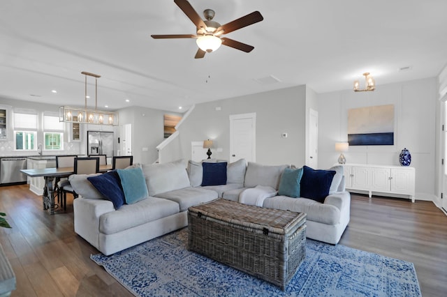 living area with ceiling fan with notable chandelier, stairway, recessed lighting, and dark wood-style floors