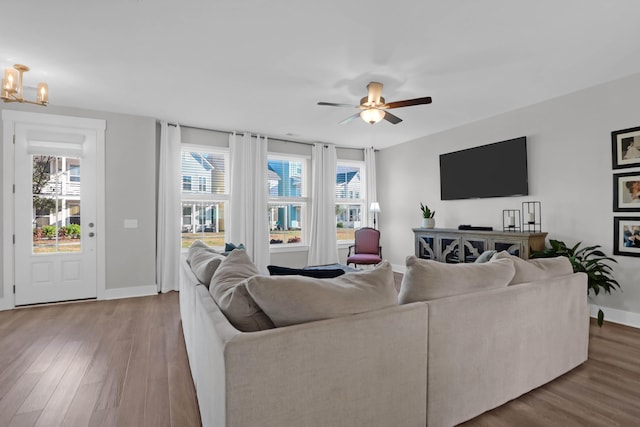 living area with baseboards, wood finished floors, and ceiling fan with notable chandelier