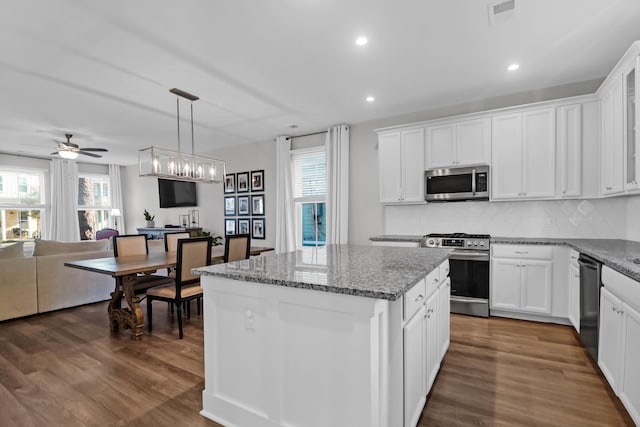 kitchen with light stone countertops, a kitchen island, dark wood finished floors, appliances with stainless steel finishes, and open floor plan