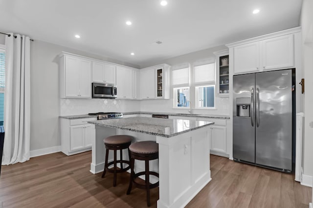 kitchen with a sink, a center island, white cabinetry, appliances with stainless steel finishes, and glass insert cabinets