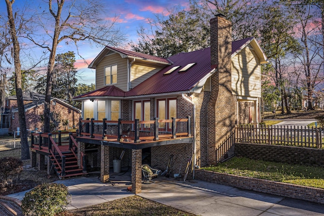 view of front facade with brick siding, a chimney, metal roof, a deck, and stairs