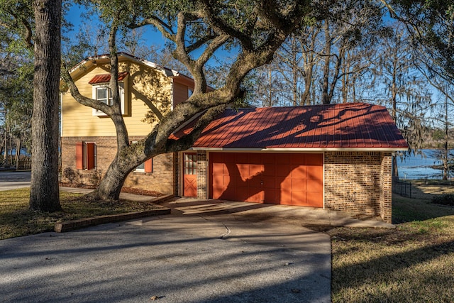 view of front of house featuring a garage, metal roof, concrete driveway, and brick siding