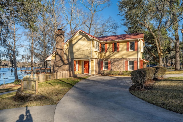 view of front of property with brick siding, a chimney, a front yard, fence, and driveway