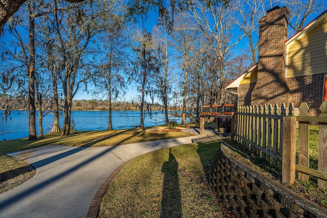 surrounding community featuring a water view, fence, and a lawn