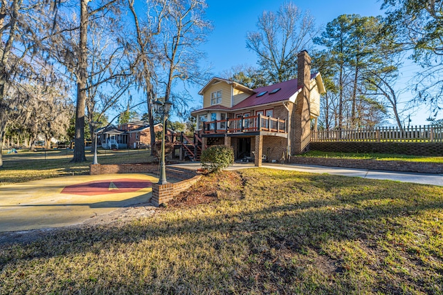 exterior space featuring brick siding, a yard, metal roof, fence, and a deck