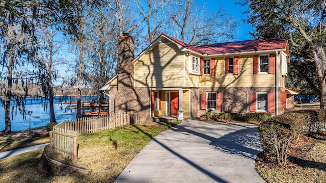 view of front facade with brick siding, a water view, fence, driveway, and a chimney