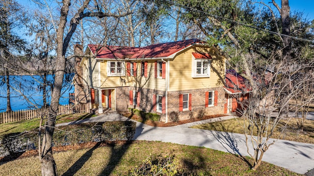 colonial house featuring brick siding, a chimney, concrete driveway, fence, and a front lawn