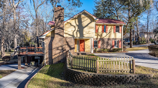 view of front facade featuring a fenced front yard, brick siding, a chimney, driveway, and a wooden deck