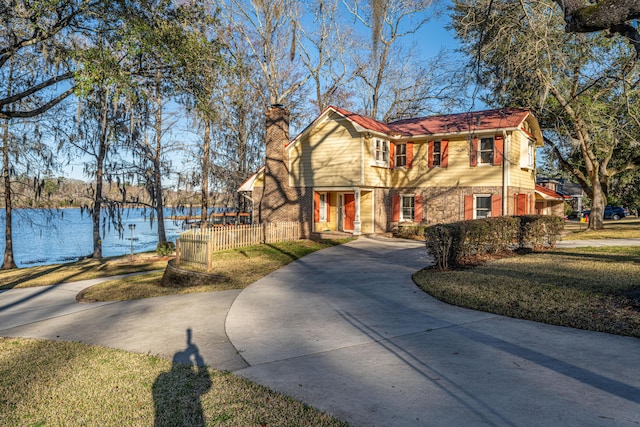 view of front of property with concrete driveway, a chimney, a water view, fence, and a front yard