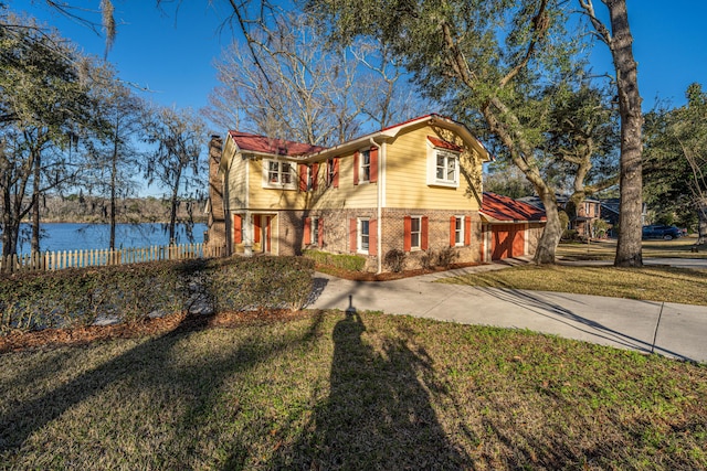 view of front of house with brick siding, a water view, a front lawn, and fence