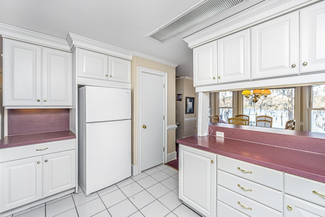 kitchen featuring crown molding, light tile patterned floors, dark countertops, freestanding refrigerator, and white cabinets