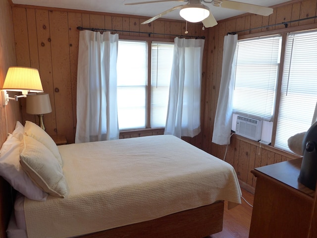bedroom with a ceiling fan, wood walls, multiple windows, and wood finished floors