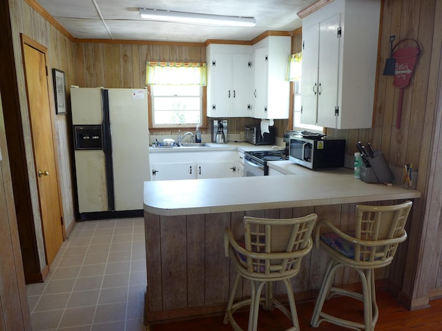 kitchen featuring electric range, wooden walls, light countertops, stainless steel microwave, and white fridge with ice dispenser