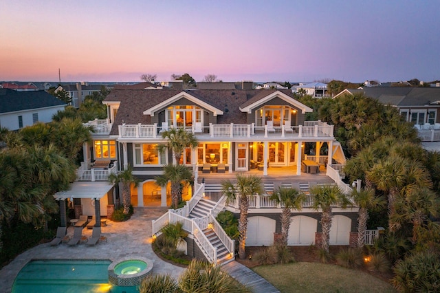 back house at dusk featuring a swimming pool with hot tub, a balcony, and a patio