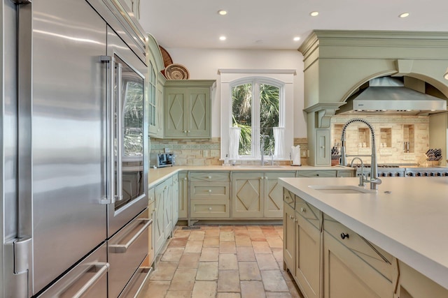 kitchen with built in fridge, wall chimney exhaust hood, and tasteful backsplash