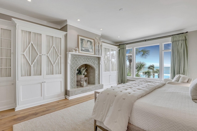 bedroom with a tile fireplace, a water view, light hardwood / wood-style flooring, and crown molding