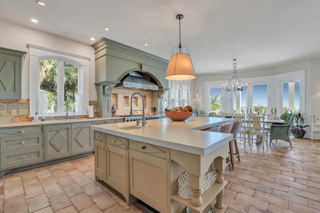 kitchen with sink, backsplash, an island with sink, a chandelier, and pendant lighting