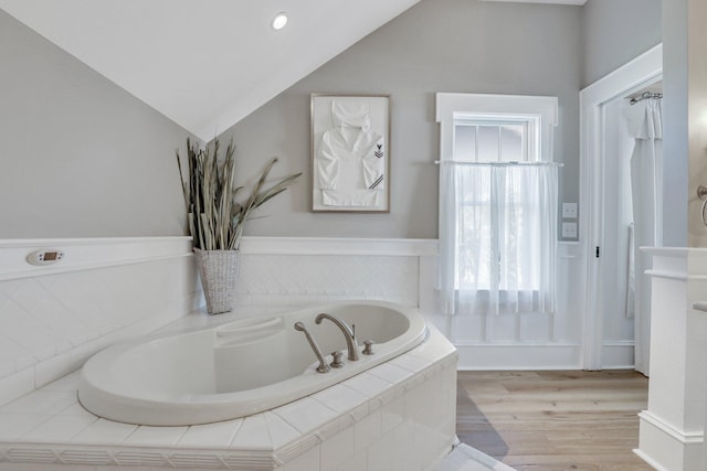 bathroom with hardwood / wood-style flooring, vaulted ceiling, and tiled tub