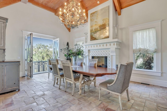 dining room featuring beam ceiling, an inviting chandelier, high vaulted ceiling, a tiled fireplace, and wood ceiling