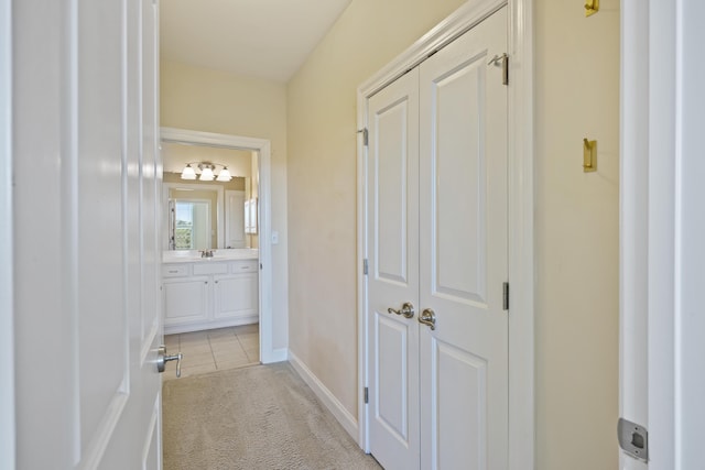 hall featuring a sink, baseboards, light colored carpet, and light tile patterned floors