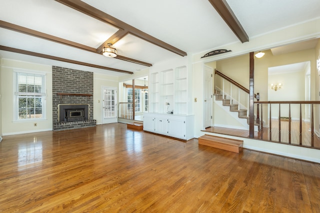 unfurnished living room with hardwood / wood-style floors, beamed ceiling, brick wall, and a brick fireplace