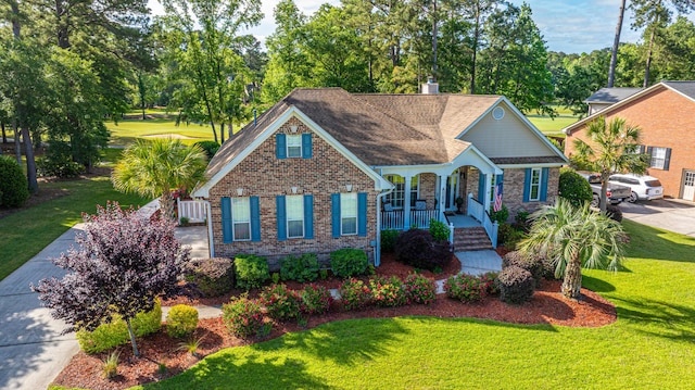 view of front of home featuring covered porch, a chimney, a front yard, and brick siding