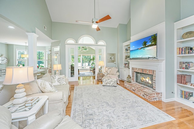 living area with built in features, a brick fireplace, ceiling fan, high vaulted ceiling, and light wood-style flooring