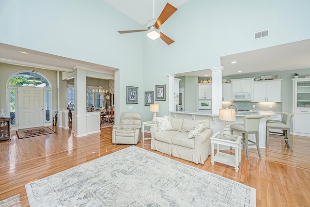 living room featuring decorative columns, high vaulted ceiling, visible vents, and light wood-style floors
