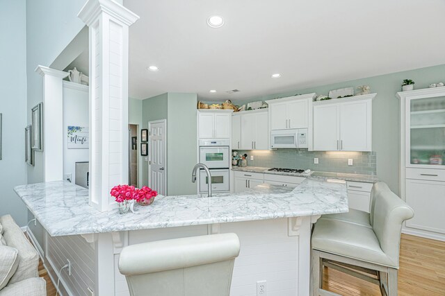 kitchen with light wood-style floors, a kitchen breakfast bar, a peninsula, and white appliances