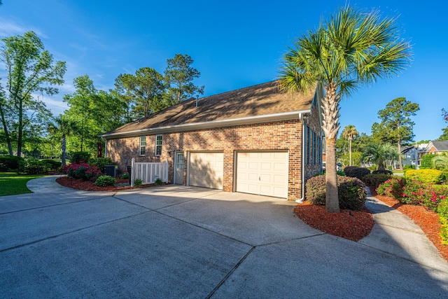 view of side of property featuring fence, an attached garage, concrete driveway, and brick siding