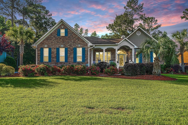 view of front of house with a yard, a porch, and brick siding