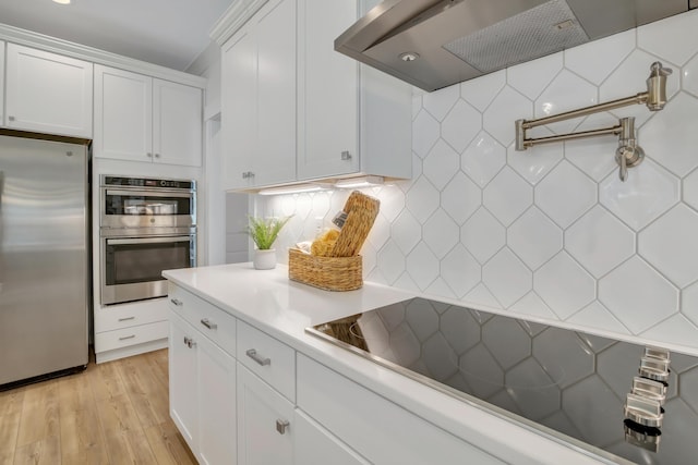 kitchen with backsplash, white cabinets, light hardwood / wood-style flooring, wall chimney exhaust hood, and stainless steel appliances