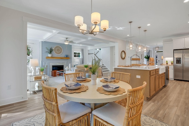 dining space with coffered ceiling, ceiling fan with notable chandelier, beam ceiling, a fireplace, and light hardwood / wood-style floors