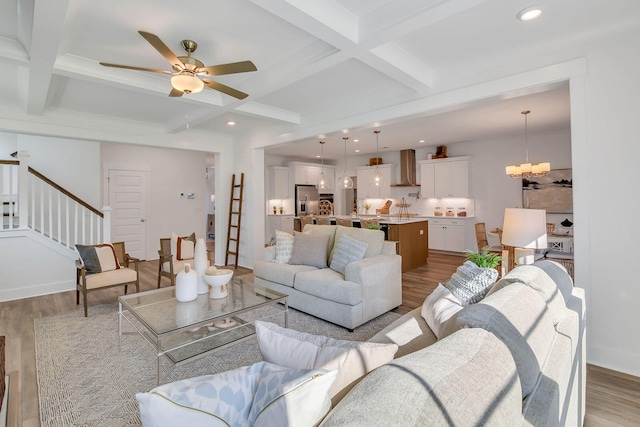 living room featuring beam ceiling, coffered ceiling, ceiling fan with notable chandelier, and light wood-type flooring