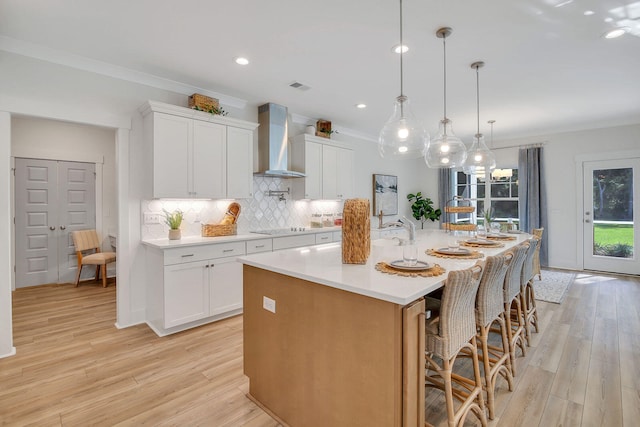 kitchen featuring white cabinets, a large island, wall chimney exhaust hood, and light hardwood / wood-style floors