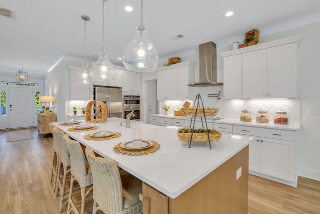 kitchen featuring white cabinetry, wall chimney exhaust hood, a spacious island, and appliances with stainless steel finishes