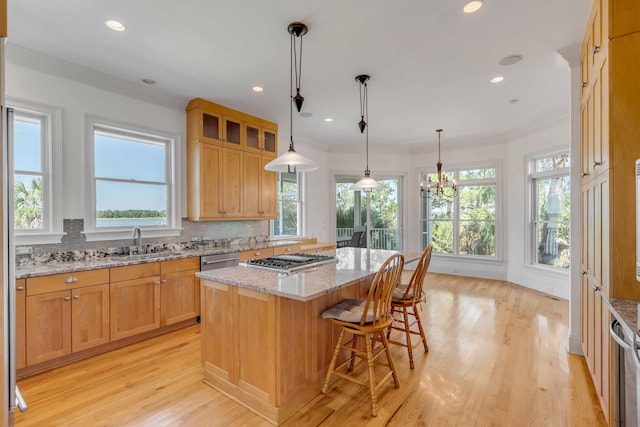 kitchen featuring sink, light hardwood / wood-style flooring, backsplash, a center island, and light stone countertops