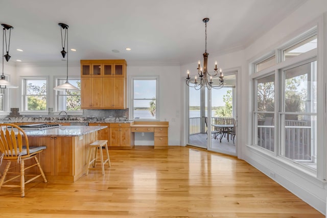 kitchen with hanging light fixtures, tasteful backsplash, a kitchen bar, light stone countertops, and light hardwood / wood-style floors