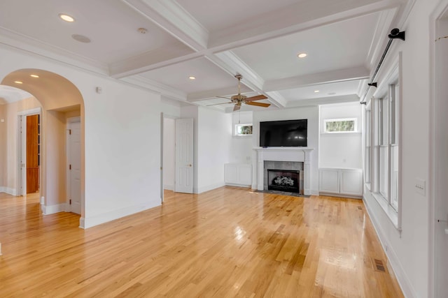 unfurnished living room featuring ceiling fan, beamed ceiling, light hardwood / wood-style flooring, coffered ceiling, and crown molding