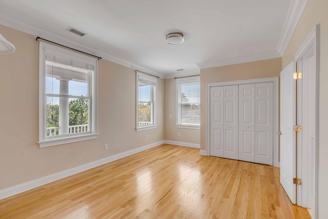 unfurnished bedroom featuring a closet, light wood-type flooring, ornamental molding, and multiple windows