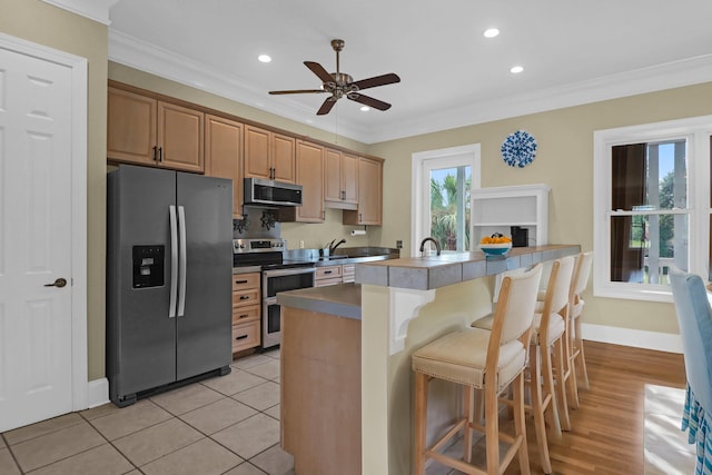 kitchen featuring a kitchen breakfast bar, stainless steel appliances, light tile patterned floors, ornamental molding, and ceiling fan