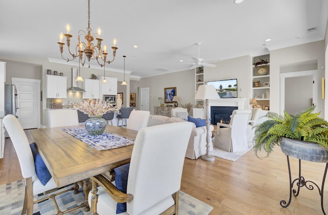 345 Turnstone St, Mount Pleasant, SC 29464 - dining room with crown molding, a glass covered fireplace, ceiling fan with notable chandelier, light wood-style flooring, and built in features