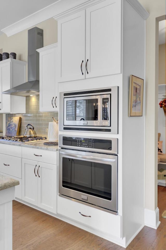 345 Turnstone St, Mount Pleasant, SC 29464 - kitchen with backsplash, white cabinetry, wall chimney exhaust hood, appliances with stainless steel finishes, and light wood-style flooring
