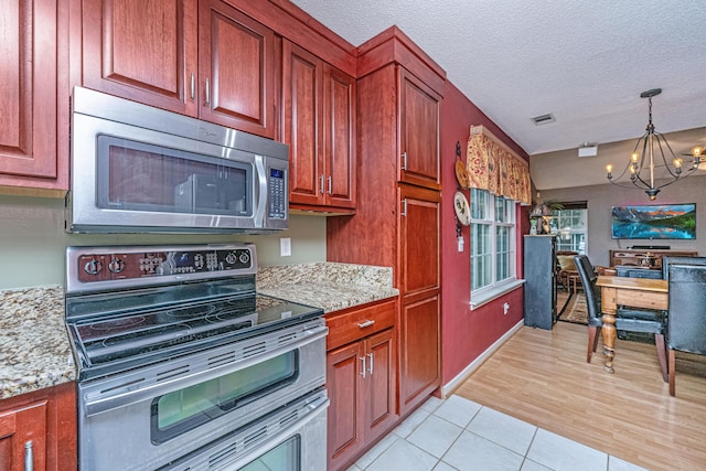 kitchen featuring stainless steel appliances, light tile patterned flooring, light stone countertops, pendant lighting, and a notable chandelier