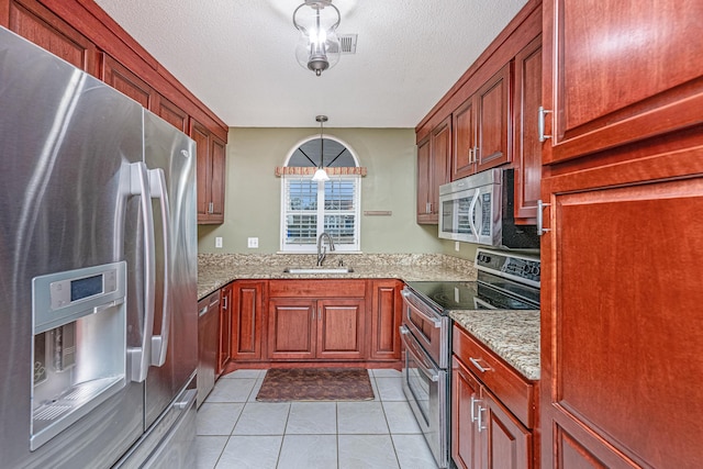 kitchen featuring sink, light stone counters, light tile patterned floors, hanging light fixtures, and appliances with stainless steel finishes